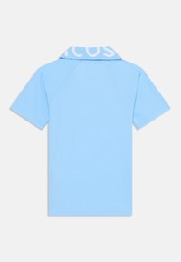 Chemise polo bleu clair avec une texture douce, arborant un logo blanc contrastant au niveau du col et des manches courtes. Vue de dos affichée.