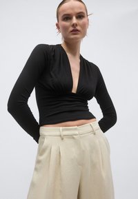 Μαύρο τοπ με μακριά μανίκια και λαιμόκοψη V, με σούρα στη μέση, σε συνδυασμό με εκρού, ψηλόμεσο παντελόνι με πιέτες.