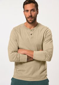 Beige Langarmshirt mit Rundhalsausschnitt und einer zwei-Knopf-Leiste. Es hat eine weiche Textur und eine leicht taillierte Passform.