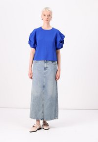 Blue puff-sleeve top with a textured finish paired with a long, light blue denim skirt. Beige shoes with a buckle detail complete the look.