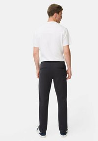 Witte kortemouwenshirt, zwarte elastische taillebroek, slim fit, gladde stof, twee achterzakken met banden, gedragen met casual sneakers.