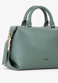 Borsa a tracolla in pelle verde con texture a grana, hardware dorato, due manici corti e chiusura con zip. Il logo è discretamente impresso sulla parte frontale.