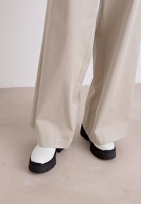 Botine albe chunky, cu talpă de cauciuc neagră, asortate cu pantaloni largi de un bej deschis. Textură netedă, detalii minime.