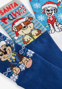 Tres pares de calcetines coloridos con perros de dibujos animados en gorros de Santa. Los diseños incluyen rayas, copos de nieve y elementos de texto festivos.