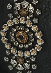 Superficie in pelle nera con motivi circolari di accenti metallici, includendo oro, argento e cristalli, con disegni floreali.