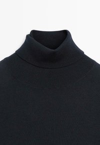 Svart polotröja med ribbat mönster. Den höga kragen sitter tight, och tyget verkar mjukt och elastiskt.