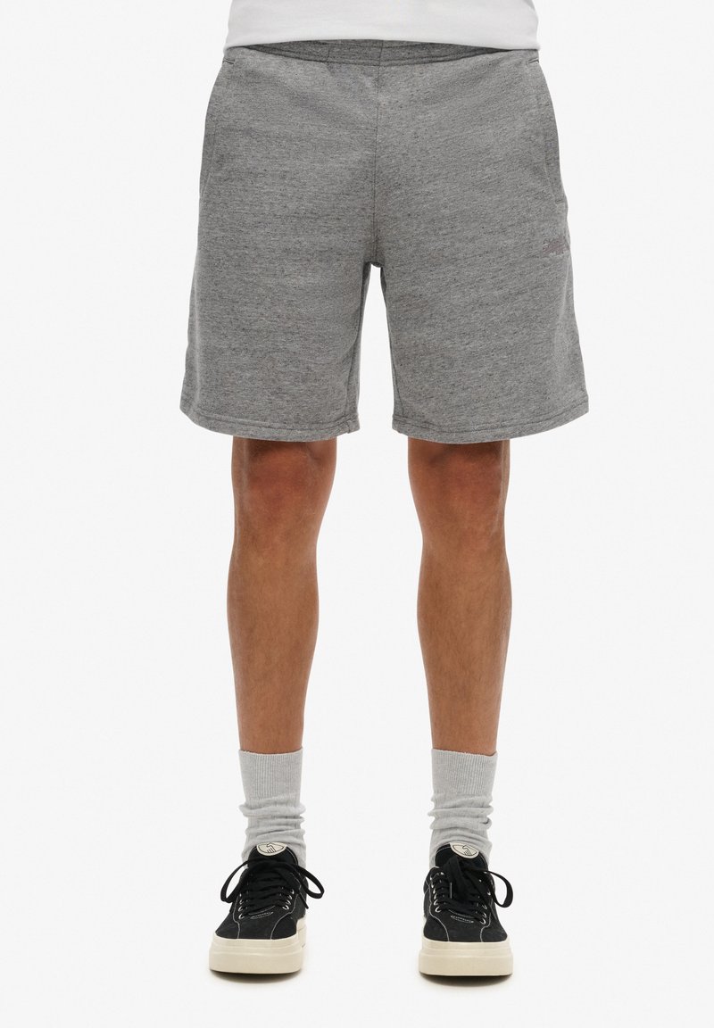 Shorts deportivos grises hechos de un tejido suave, con una cintura elástica y corte recto. Combinados con zapatillas negras y calcetines grises.
