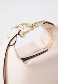 Bolso de mano de color rosa suave con una textura lisa, que presenta un cierre de hardware dorado y detalles de cremallera. La correa está acentuada con un ribete negro.
