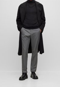 Černý vlněný kabát, upnutý černý rolák, šedé elegantní kalhoty a černé kožené boty. Vlastnosti zahrnují design do V a jemnou strukturu.