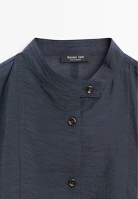 Mörkblå skjorta med mandarinkrage, tre synliga mörka knappar och etikett "Massimo Dutti Made in Morocco" på insidan av kragen.