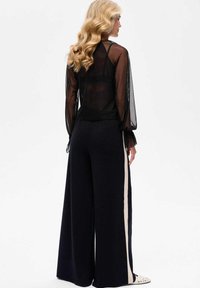 Czarna siateczkowa bluzka z długim rękawem i przezroczystym tyłem. Połączona z szerokimi granatowymi spodniami z kremowym paskiem po bokach. Widoczne detale textured.