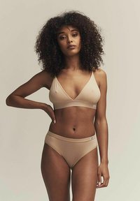 Soutien-gorge en tissu nude avec un design en V et des bretelles ajustables, associé à un bas de bikini assorti. Texture lisse, détails minimaux.