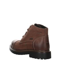 Botas de cuero marrón hasta el tobillo con una puntera redonda, diseño de cordones, acentos de costura y suela de goma gruesa. Logo de la marca en el costado.