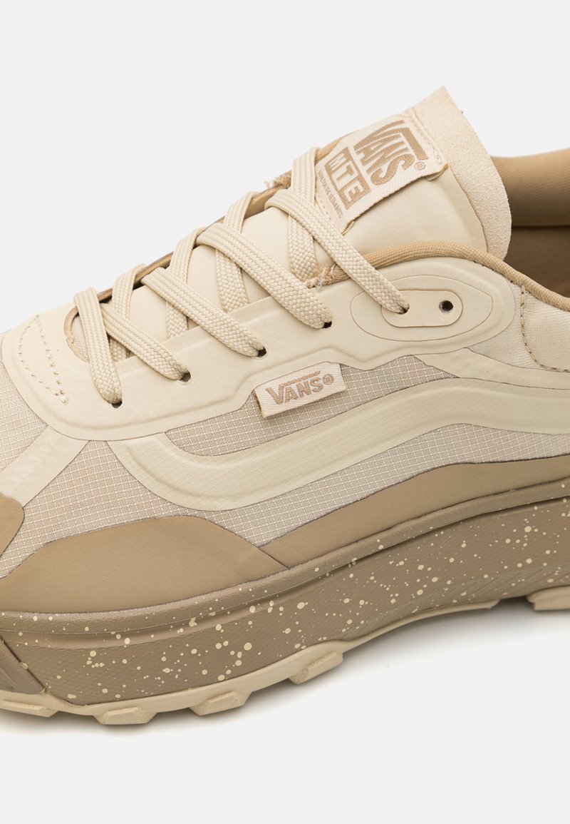 Beżowy canvas sneaker z teksturowaną powierzchnią, tonalnym ściegiem, oznakowaną język i plamistą podeszwą dla lepszej przyczepności i stylu.