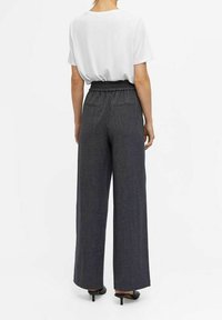 Haut blanc à manches courtes associé à un pantalon taille haute à jambes larges gris foncé ; le pantalon présente des poches latérales et un tissu légèrement texturé.