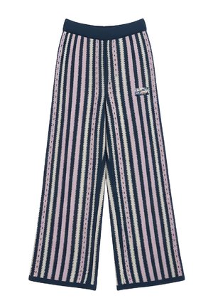 Man wearing wide-leg pants with vertical navy, pink, and white stripes, paired with white sneakers and a white sleeveless top.