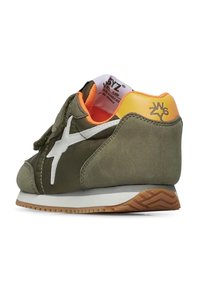 Sneaker verde in suede con accenti bianchi, fodera arancione e suola marrone texture. Presenta un logo sul tallone e una fascia in velcro.