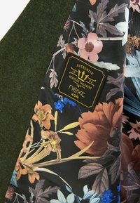 Tissu en laine verte avec une doublure noire à motif floral. Présente une étiquette dorée indiquant "Authentic Heritage Tailoring 1982 next 40R".