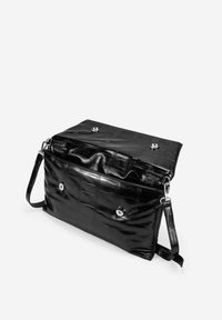 Bolso negro de piel acolchada con forma plana, herrajes plateados, cierres a presión y una correa de hombro desmontable. Detalle de superficie texturizada.