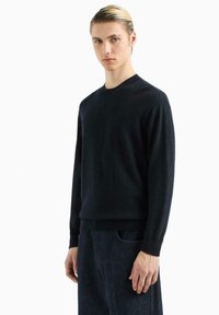 Maglione lavorato a maglia blu navy con motivo texturizzato, scollatura tonda e polsini e orlo a costine. Abbinato a pantaloni in denim scuro.