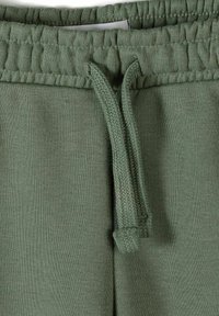 Zelený elastický pás s uvázaným copánkovým stahovacím šňůrkem na texturovaných kalhotách nebo šortkách.