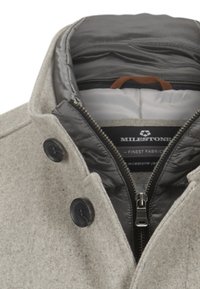 Grau melierter Wollmischmantel mit einer abnehmbaren Innenjacke, schwarzen Knöpfen und einem Reißverschluss. Das Innenfutter ist glatt und gesteppt.