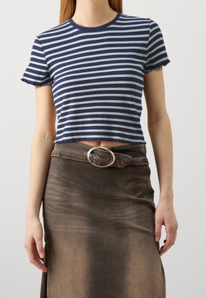 Kvinde iført en kort mørkeblå og lyseblå stribet ribstrikket T-shirt kombineret med et brunt nederdel med høj talje og en oval spænde bælte.