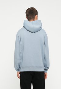Felpa con cappuccio di colore azzurro chiaro, dalla vestibilità comoda, con spalle scese e polsini a coste. Texture liscia, senza motivi o grafiche visibili.