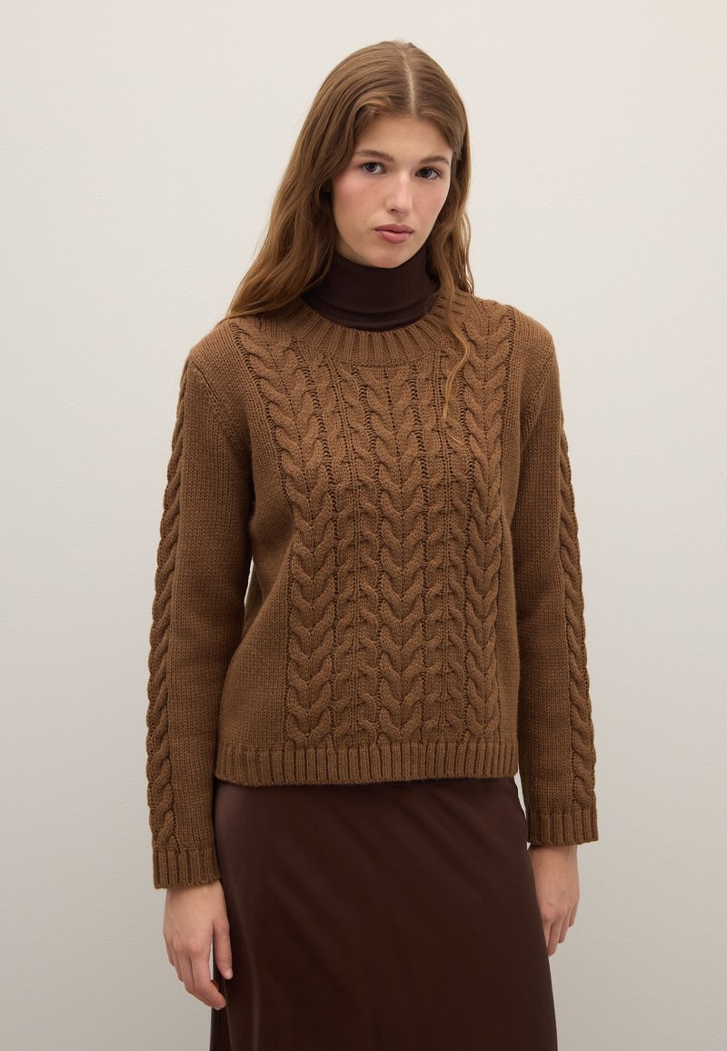 Brown cable-knit sweater with a ribbed crew neckline, textured pattern, and long sleeves, paired with a dark brown skirt.
