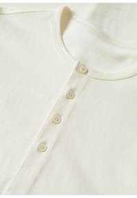 Chemise blanc cassé à manches longues avec un col rond et une patte de boutonnage devant comportant quatre petits boutons assortis.