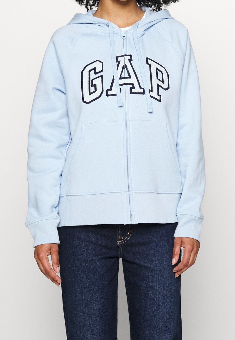 Light blue zip-up hoodie made of soft fabric, featuring black "GAP" lettering across the chest and a front kangaroo pocket.