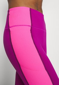 Leggings con una vita alta, caratterizzati da un design a blocchi di colore rosa e viola, texture a coste e cuciture scure a contrasto.