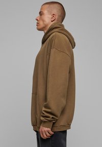 Sudadera con capucha marrón de corte holgado, con un gran bolsillo frontal, puños acanalados y textura suave, exhibida sobre un fondo neutro.