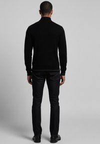 Suéter negro acanalado con cuello alto, combinado con jeans oscuros. El conjunto presenta una silueta ajustada y una textura suave. Calzado casual completa el atuendo.
