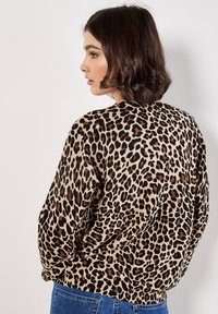 Leopard-print, lightweight sweater with a round neckline and ribbed hem. Features a smooth texture in beige, black, and brown colors.