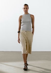 Grijze mouwloze top, beige wijde shorts met een knoop en zwarte sandalen met bandjes. Gladde texturen en neutrale kleuren.
