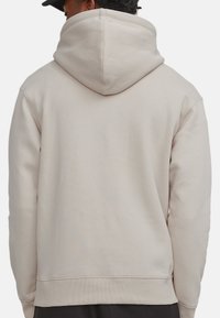 Beige Kapuzenpullover mit großer, weicher Kapuze. Hergestellt aus einem Baumwollmischgewebe. Verfügt über gerippte Bündchen und Saum für eine enge Passform.