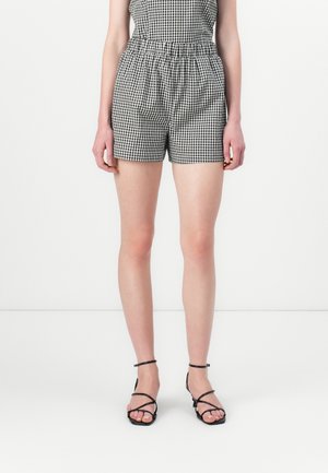 Shorts vichy noir et blanc avec une taille élastique, offrant une coupe décontractée et une texture lisse, associés à des sandales noires à brides.
