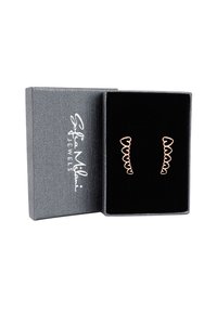 Roséguldörhängen med vågig design visade i en grå låda med svart sammet, som har en texturerad yta och vit logotyp.