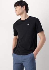 Zwarte katoenen t-shirt met een ronde hals, korte mouwen en een wit logo op de borst. Glad oppervlak, getailleerd ontwerp.