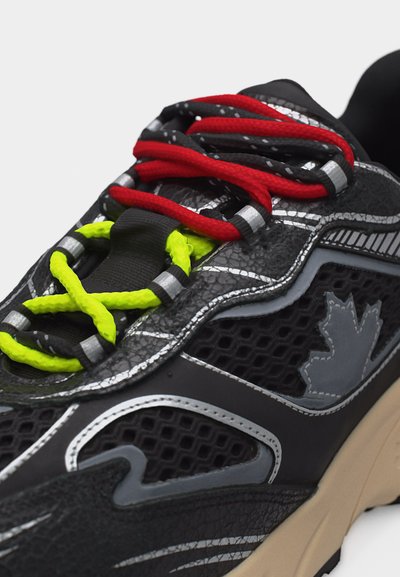 Chaussure de sport noire avec des lacets rouges et jaune néon, des détails réfléchissants argentés, et un logo de feuille d'érable sur le côté.