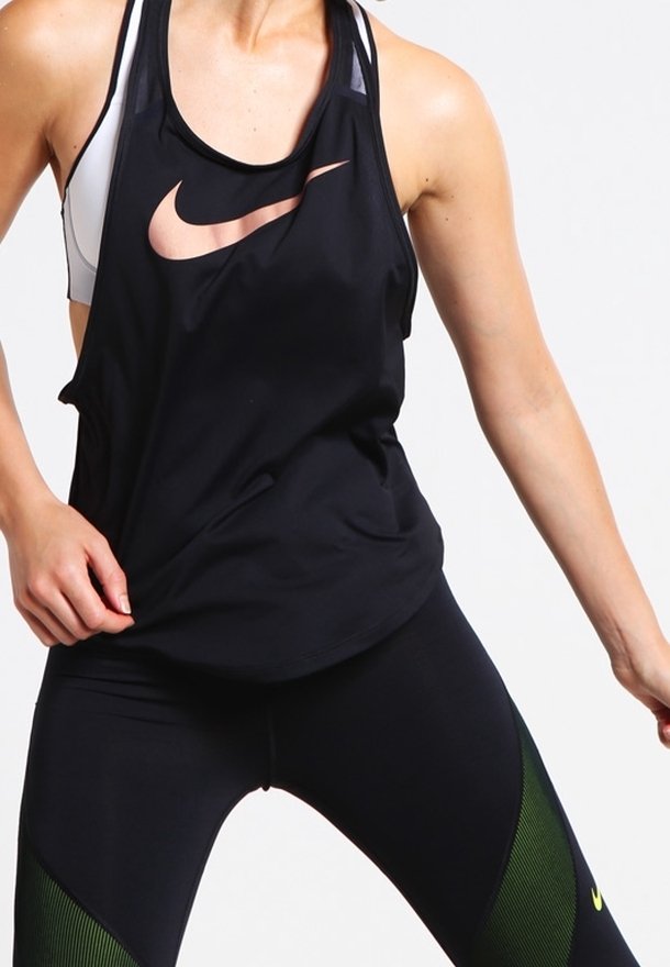 Donna che indossa un top e leggings neri Nike con pannelli verdi, mostrata in movimento su uno sfondo bianco uniforme.