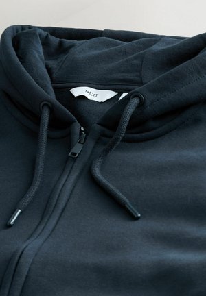 Black zip-up hoodie made of soft fabric, featuring a drawstring hood, front zipper, and a tag displaying "NEXT." Smooth texture, no visible patterns.