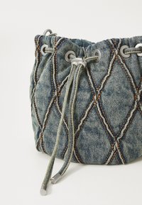 Borsa in denim con cordoncino, presenta un motivo a diamante trapuntato, occhielli argentati e cuciture arancioni a contrasto. Superficie testurizzata e spallacci regolabili.