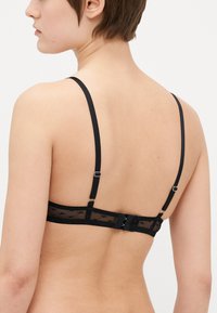Black lace bra featuring thin straps, a mesh band with a geometric pattern, and a hook-and-eye closure at the back.