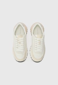 White and beige sneakers with a smooth upper, lace closures, textured accents, and a black rubber sole. Angular design with stitching details.