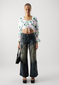 Biely kvetinový crop top s nadýchanými rukávmi a viazaným predným dielom; modré široké nohavice s vreckami; čierna kabelka; platformové topánky.