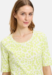 Kortærmet top i hvid med lys grøn leopardprint. Har rund halsudskæring og ribbet struktur over hele stoffet.