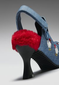 Blå denim høyhælte sko med rød lodden kant, broderi av en hane, knappet stropp og svart buet hæl på rillestøpt såle.