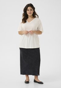 Lichtbeige V-hals t-shirt gecombineerd met een lange, donkere spijkerrok met een zijsplit, aangevuld met zwarte ballerina's. Gladde texturen overal.